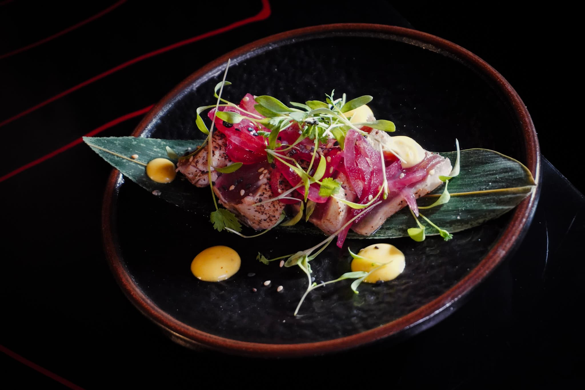 Seared tuna tataki plated with microgreens and sesame seeds.