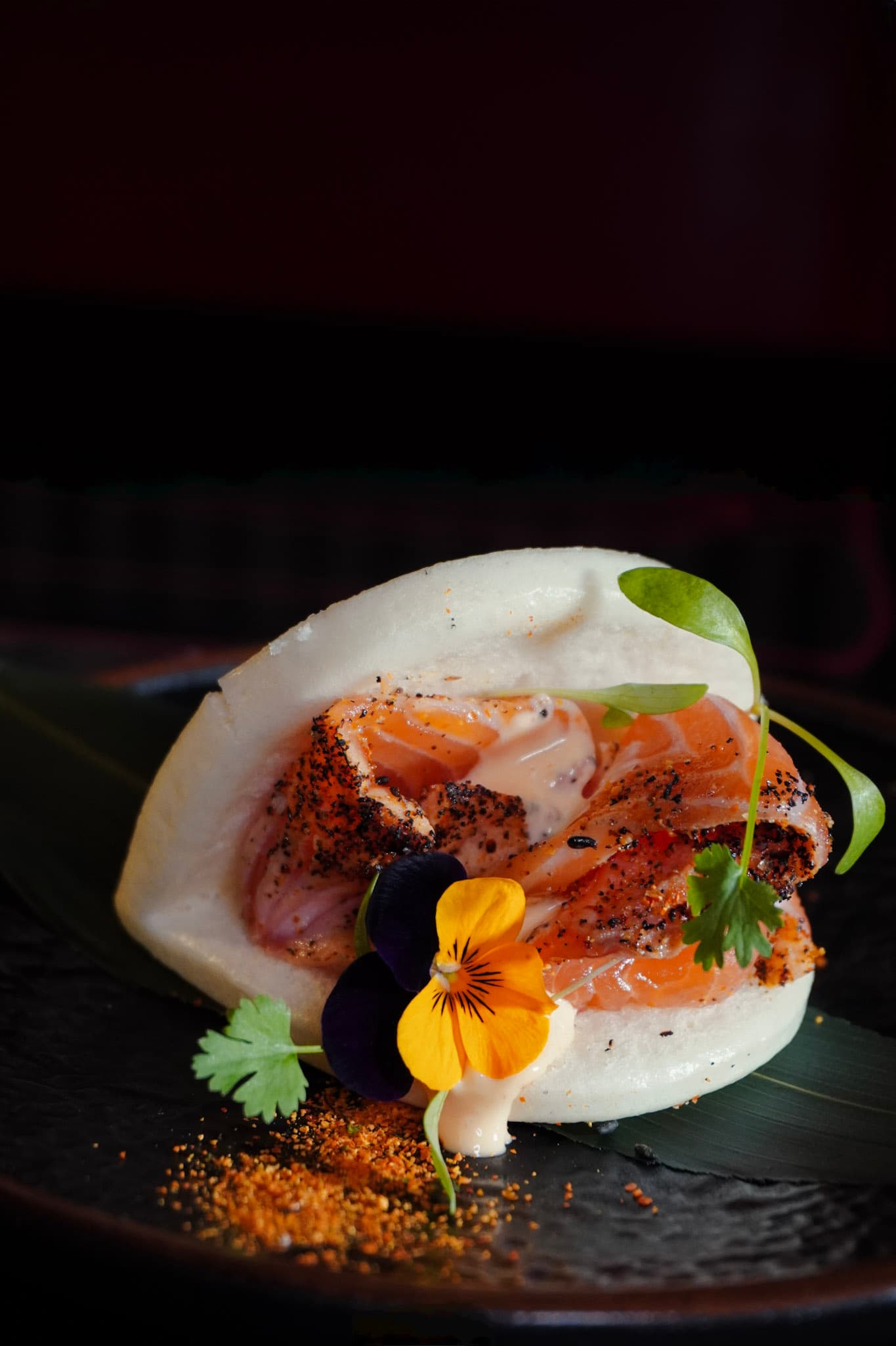 Torched salmon bao bun styled with edible flowers.