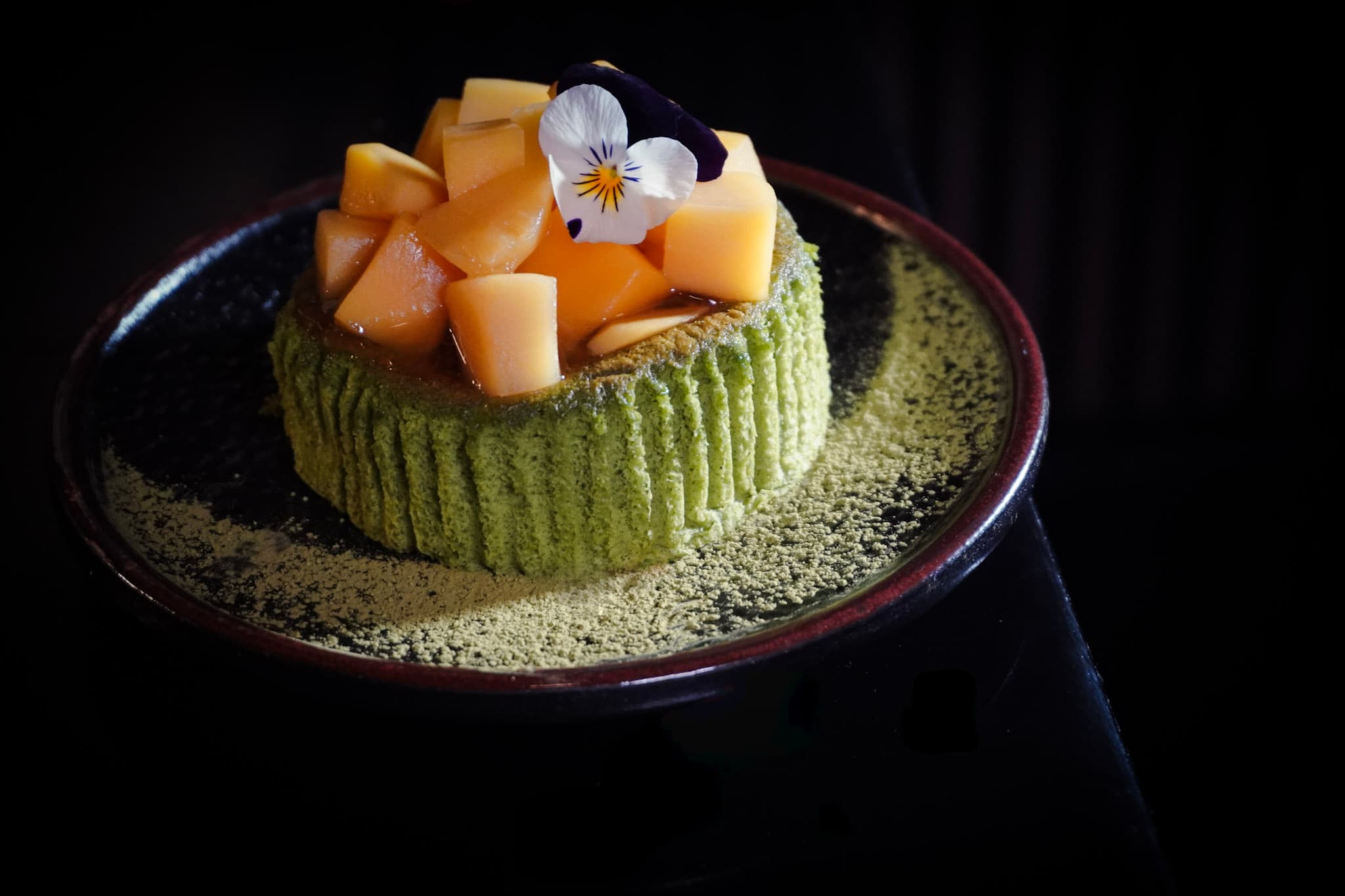 Japanese matcha cheesecake with mango-yuzu sauce and edible flowers.