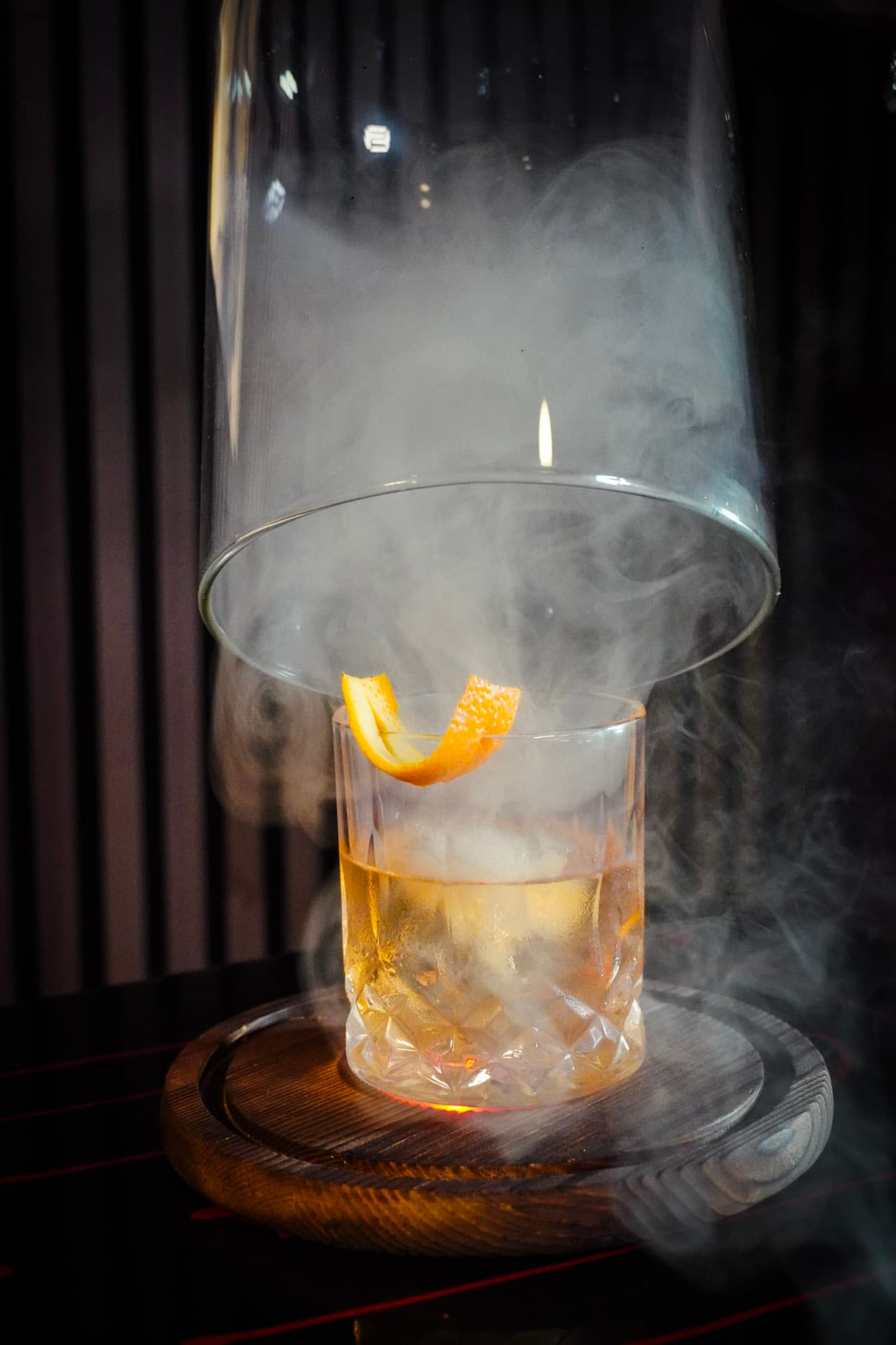 A smoky old fashioned cocktail under a glass cloche on a wooden board at Tokyo Club Sushi Speakeasy.