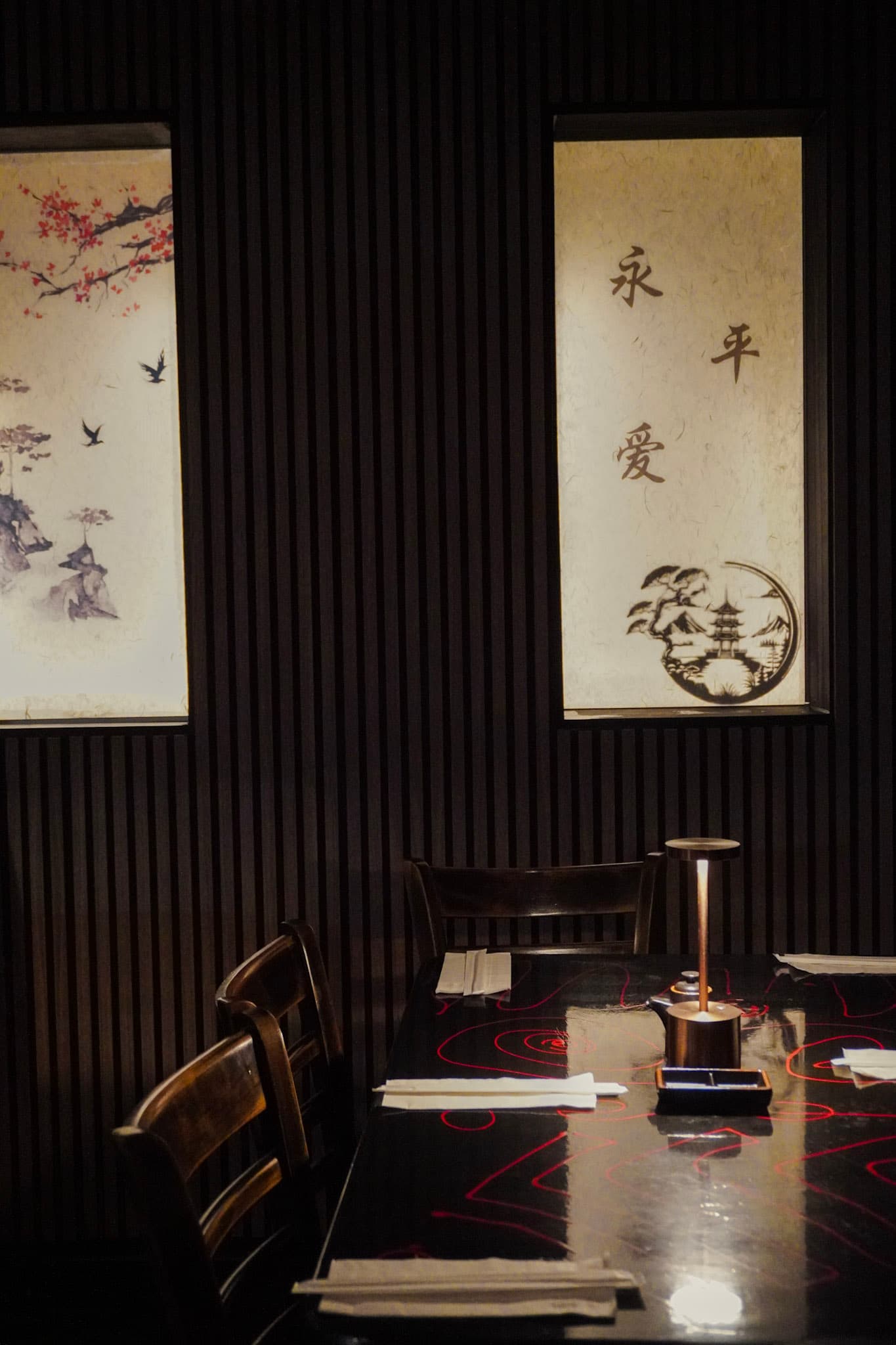 A moody table setting inside Tokyo Club Sushi Speakeasy with Japanese scroll art and dark slatted walls.