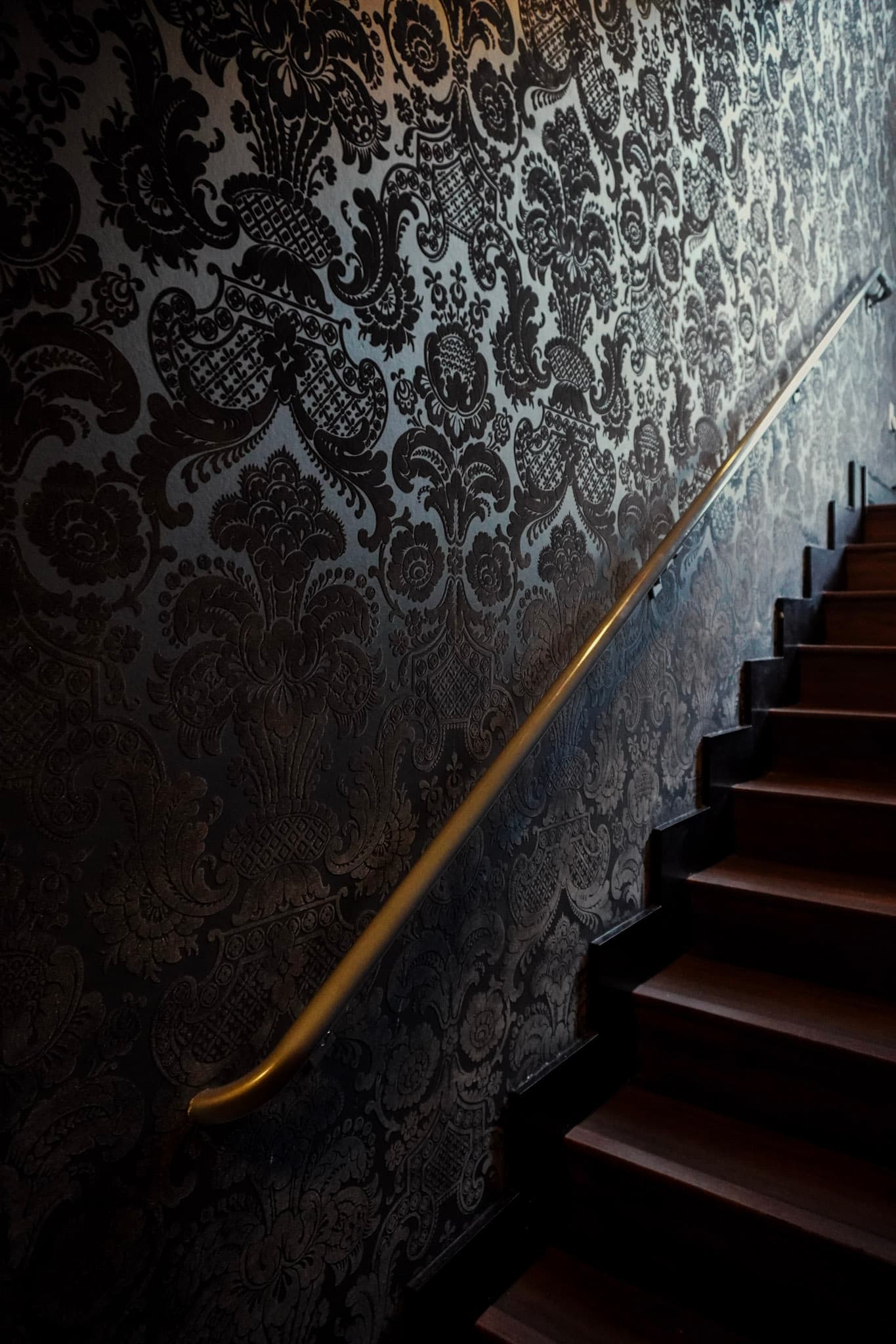 An ornate damask-wallpapered staircase with a gold handrail leading into Tokyo Club Sushi Speakeasy.