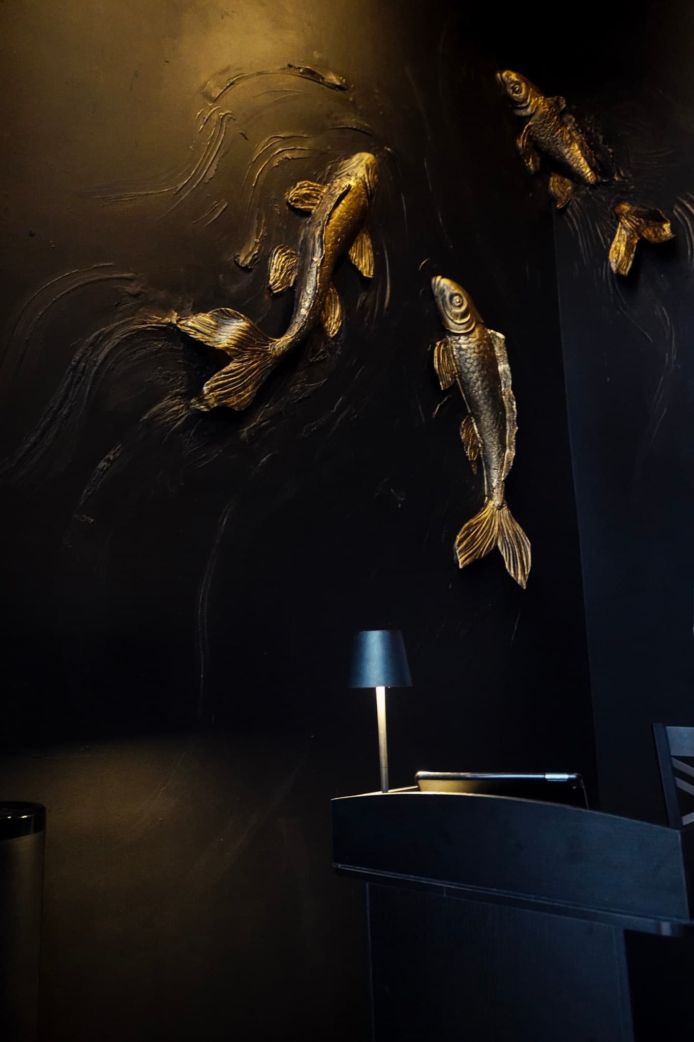 Golden koi fish sculptures swimming across a dark textured wall inside Tokyo Club Sushi Speakeasy.