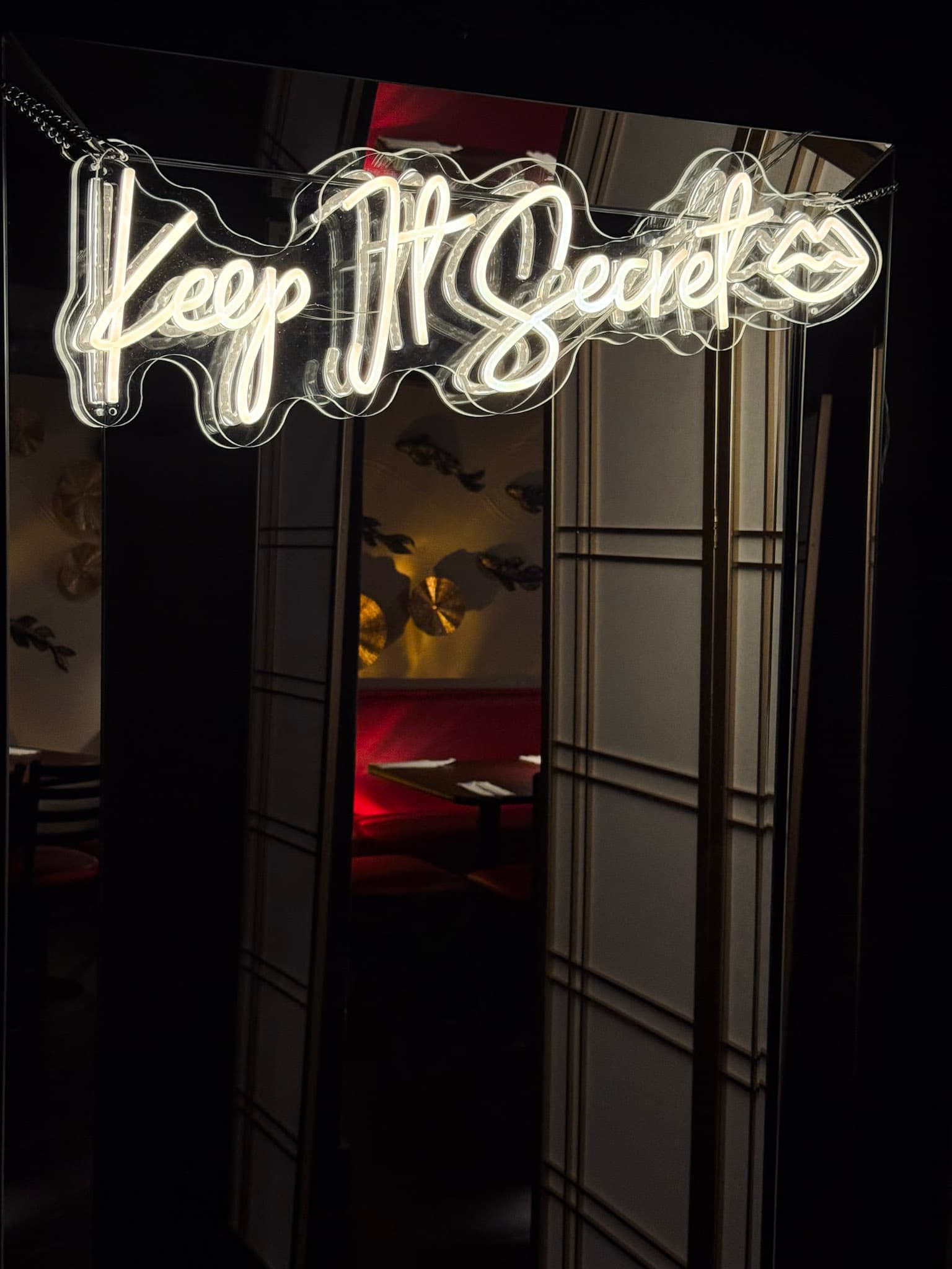 'Keep It Secret' neon sign glowing above a view into the intimate speakeasy dining room.