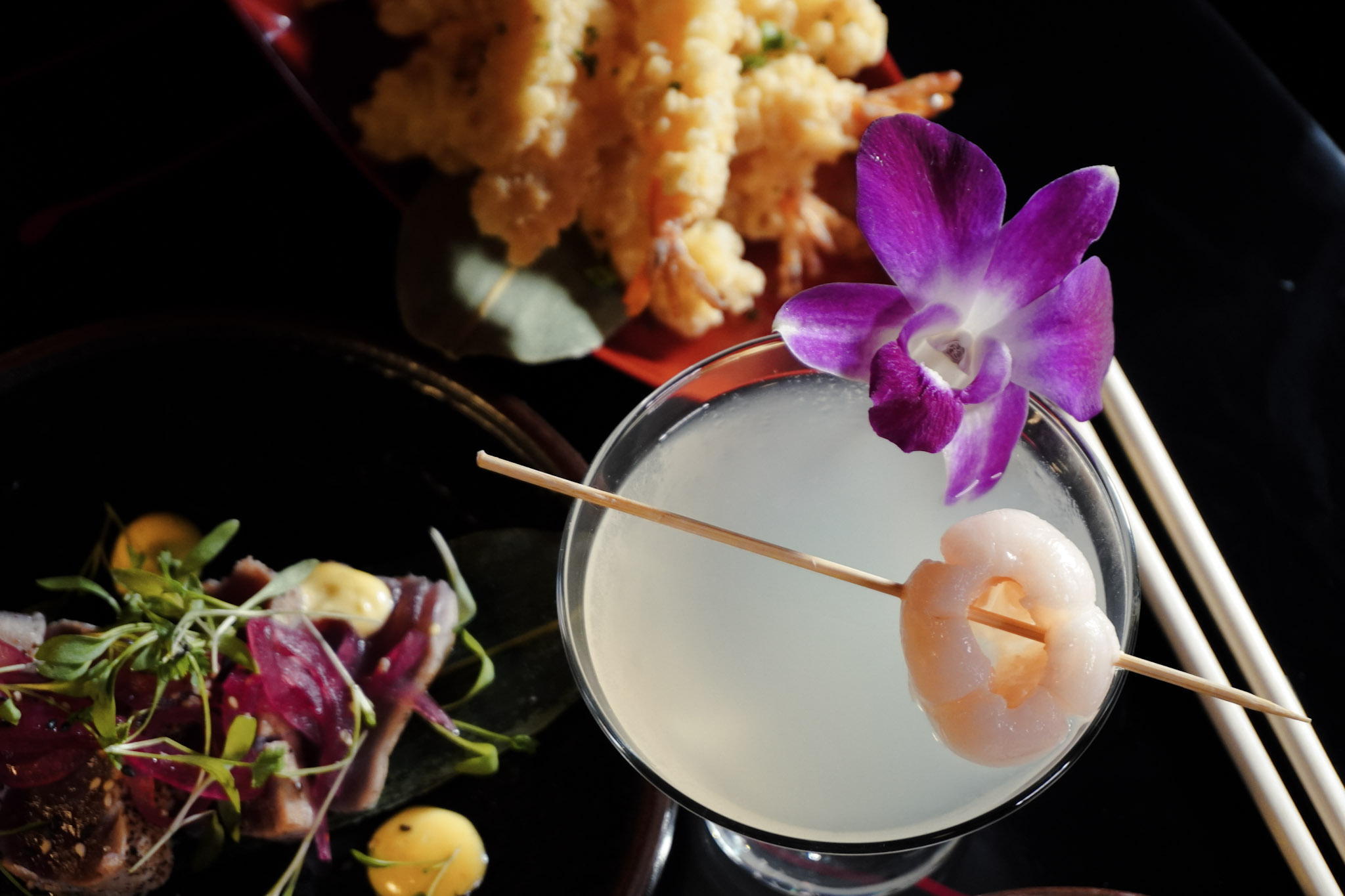 A lychee orchid cocktail in dramatic closeup with floral garnish.
