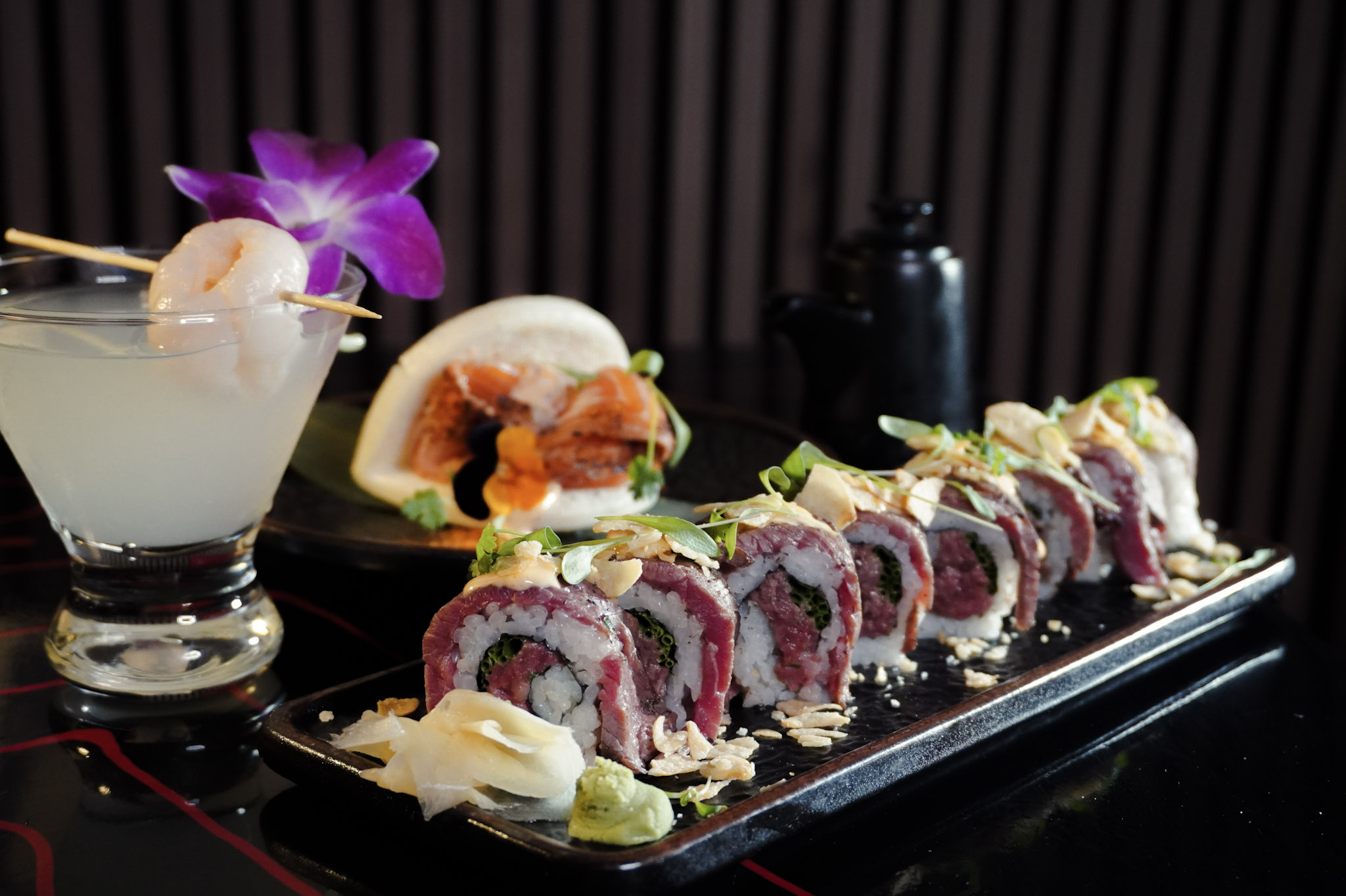 A dramatic dinner spread with beef sushi rolls, cocktails, and bao buns.